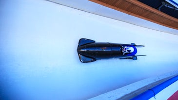 Blue multi-person bobsled speeding around a curve on an ice track