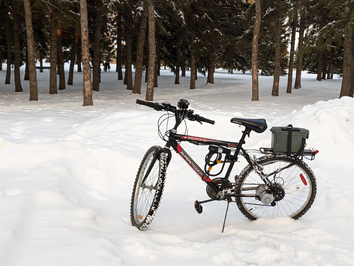 A homemade DIY e-bike parked in front of a snow-covered evergreen grove.