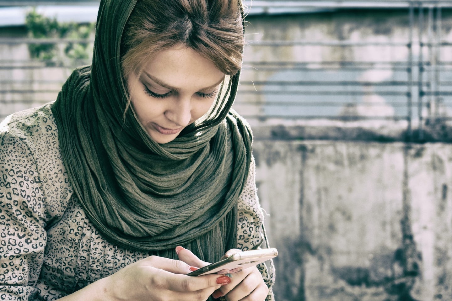 Person with brown hair, leopard-print shirt, and black scarf texting on a smartphone