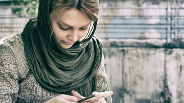 Person with brown hair, leopard-print shirt, and black scarf texting on a smartphone