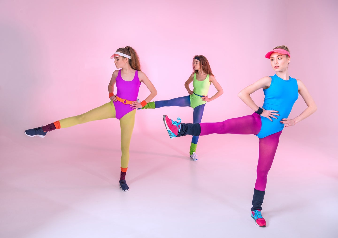 Three people in multicolored Lycra spandex exercise outfits in front of a light pink backdrop