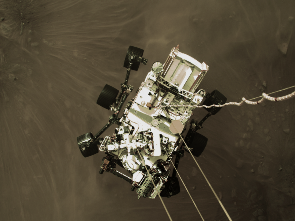 Top-down view of a six-wheeled Perseverance rover parachuting down onto Mars
