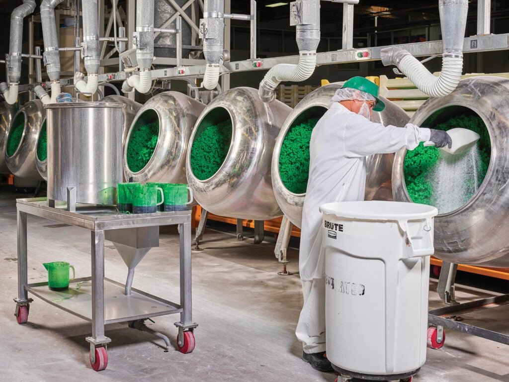 Worker on a white coat coating green jelly beans with sugar and syrup in panning department