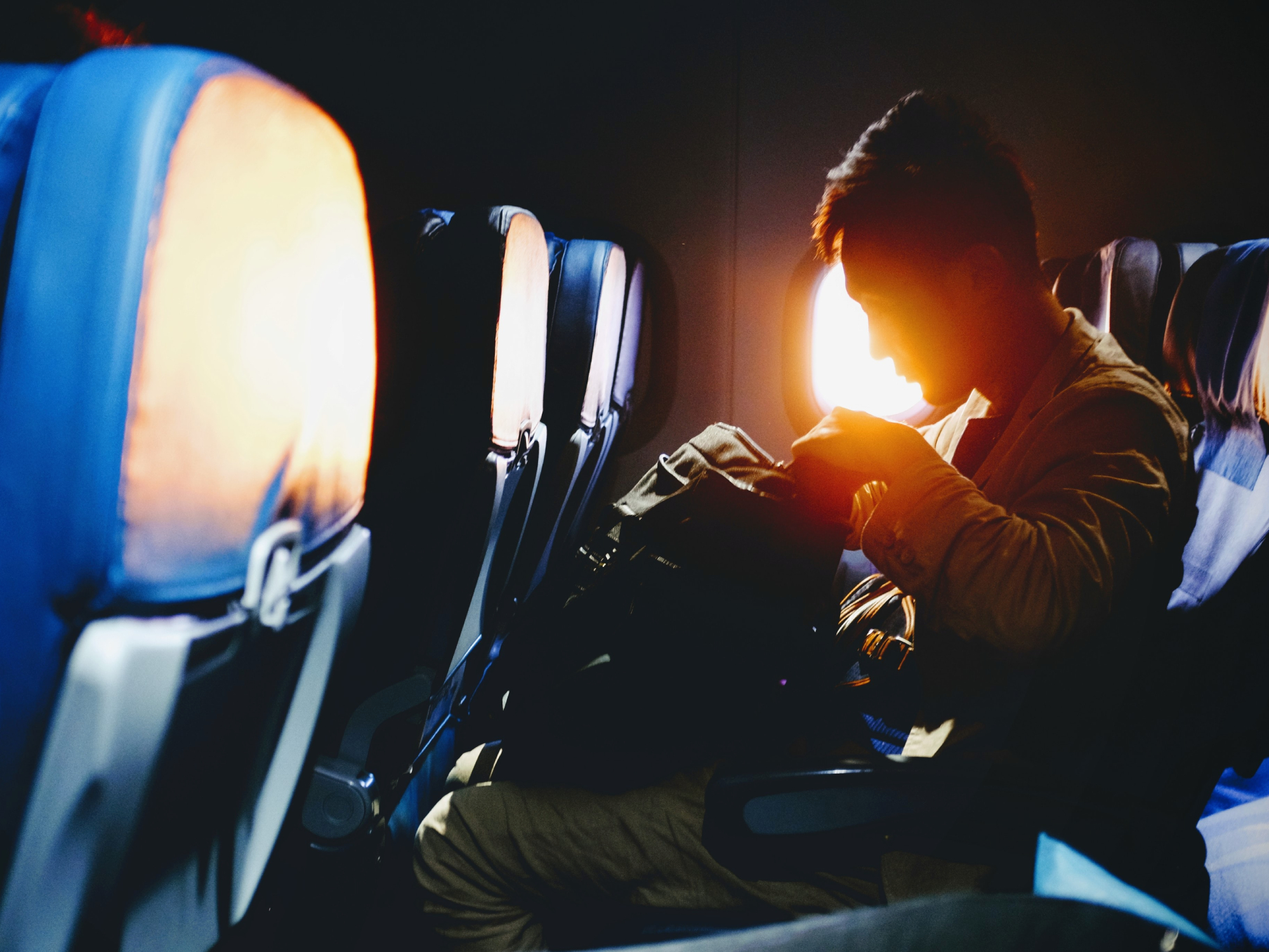 A man sitting on an airplane at sunset and looking into his backpack.