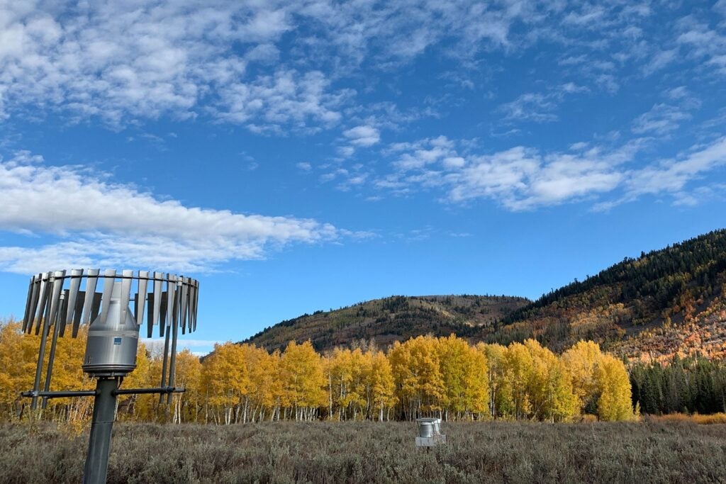 A weather station in front of a Utah mountain range dotted with yellow aspen trees