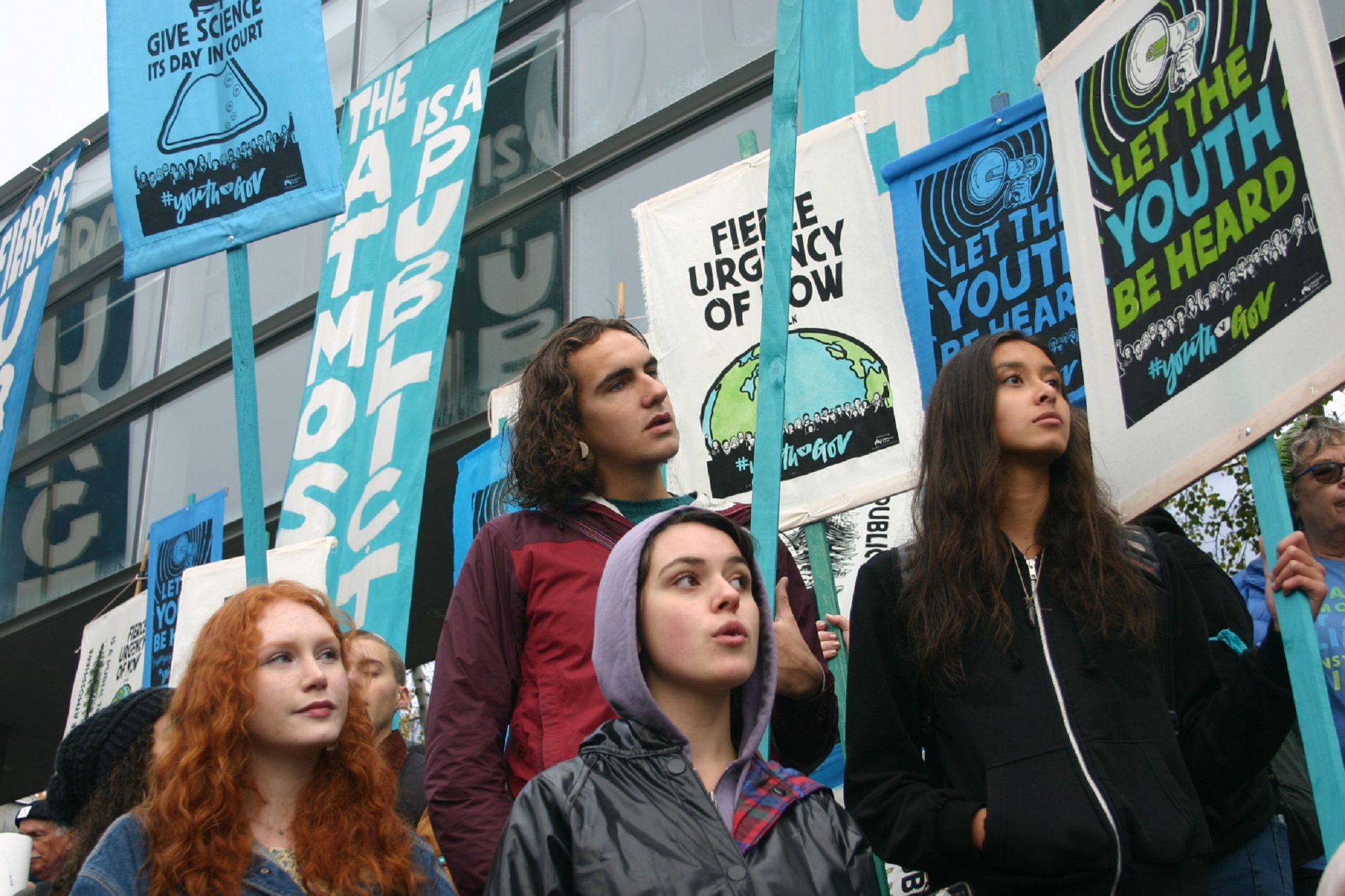 Students at a climate rally holding blue environmentalism signs on a cloudy day