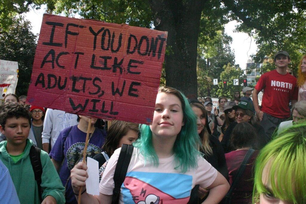 A student in a pink tshirt and green hair holding up a red climate activism sign