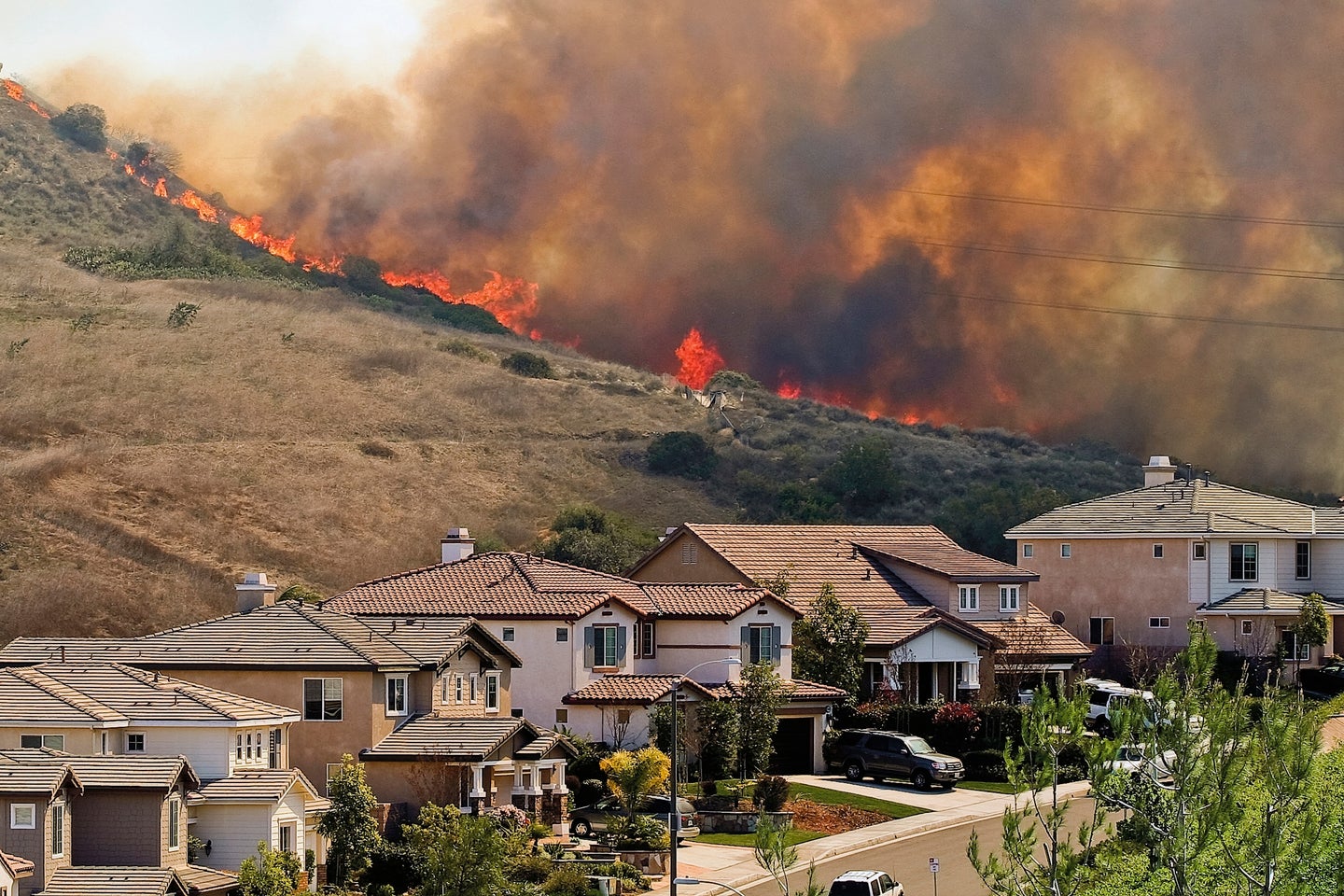 A row of suburban houses with a hill behind and an approaching wildfire over the California hills