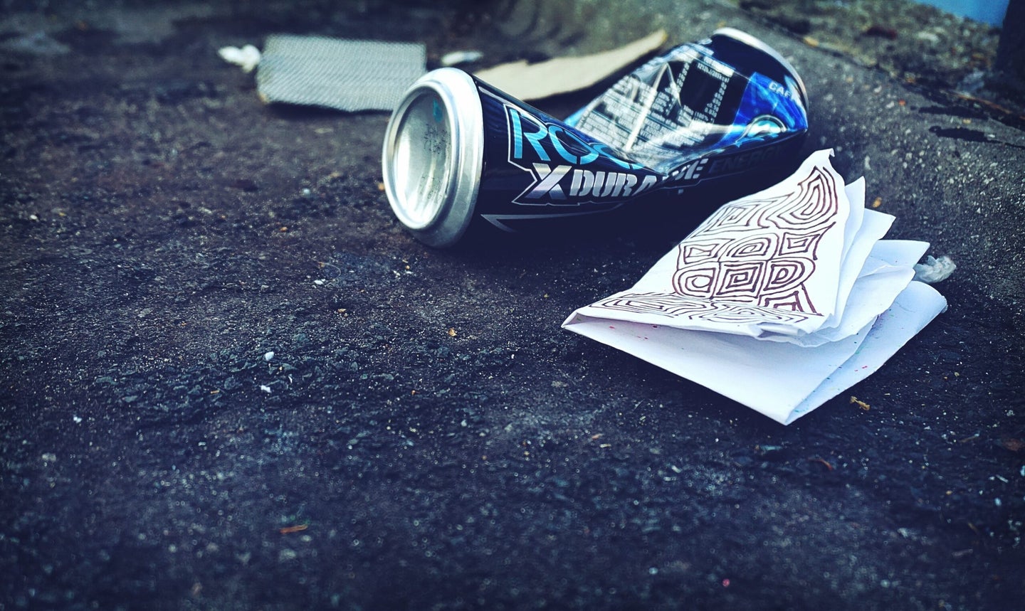 Street with trash, drink bottle, paper.