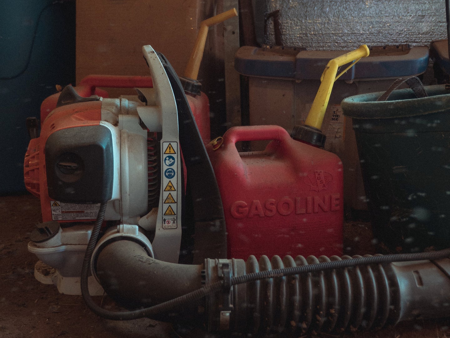 A red gasoline can in a garage or shed next to a large gas-powered leafblower.