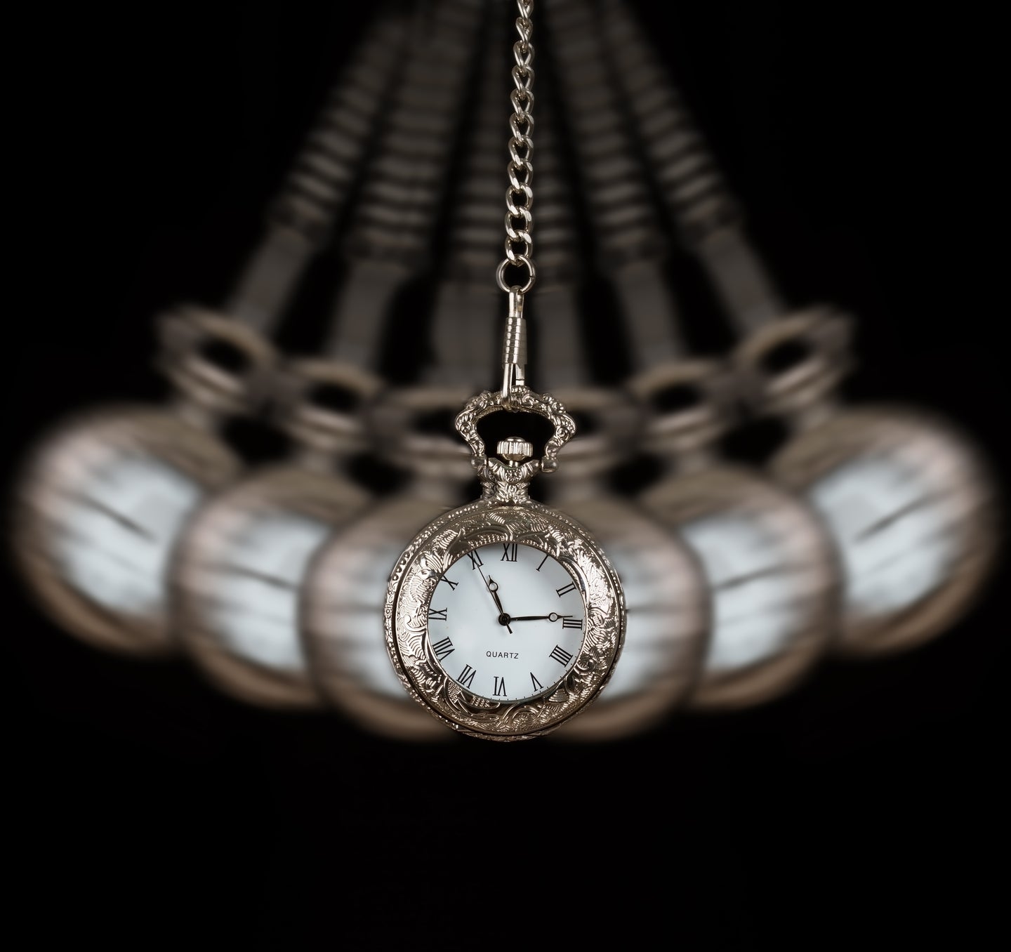 Silver pocket watch being swung on a chain on a black background to symbolize a time crystal