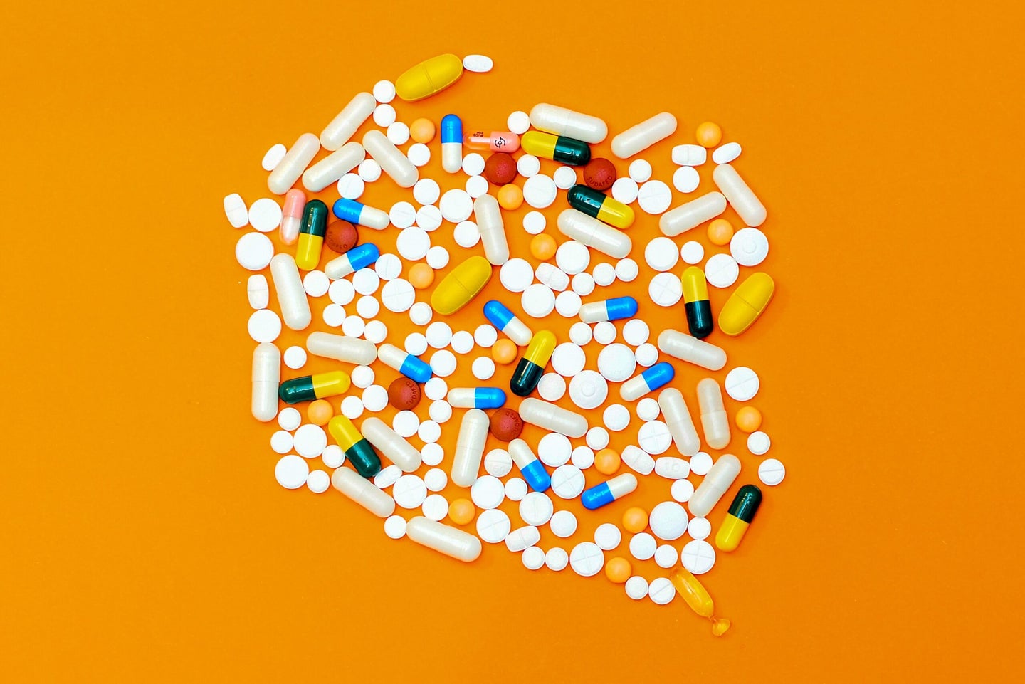 A pile of pills of various shapes and colors on an orange background. Some of these may be allergy medications.