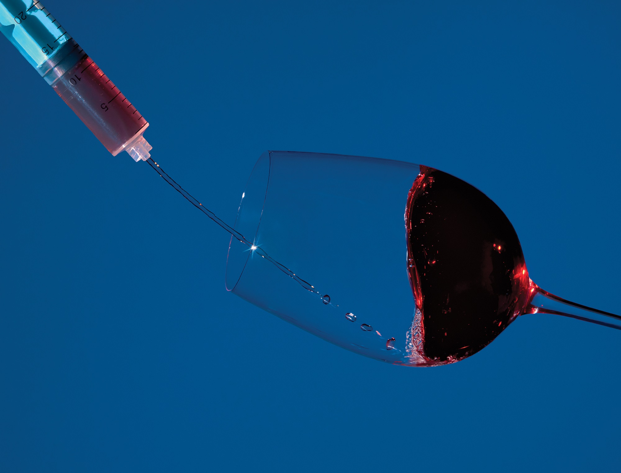 Syringe pouring red wine into a long-stem glass on a navy background