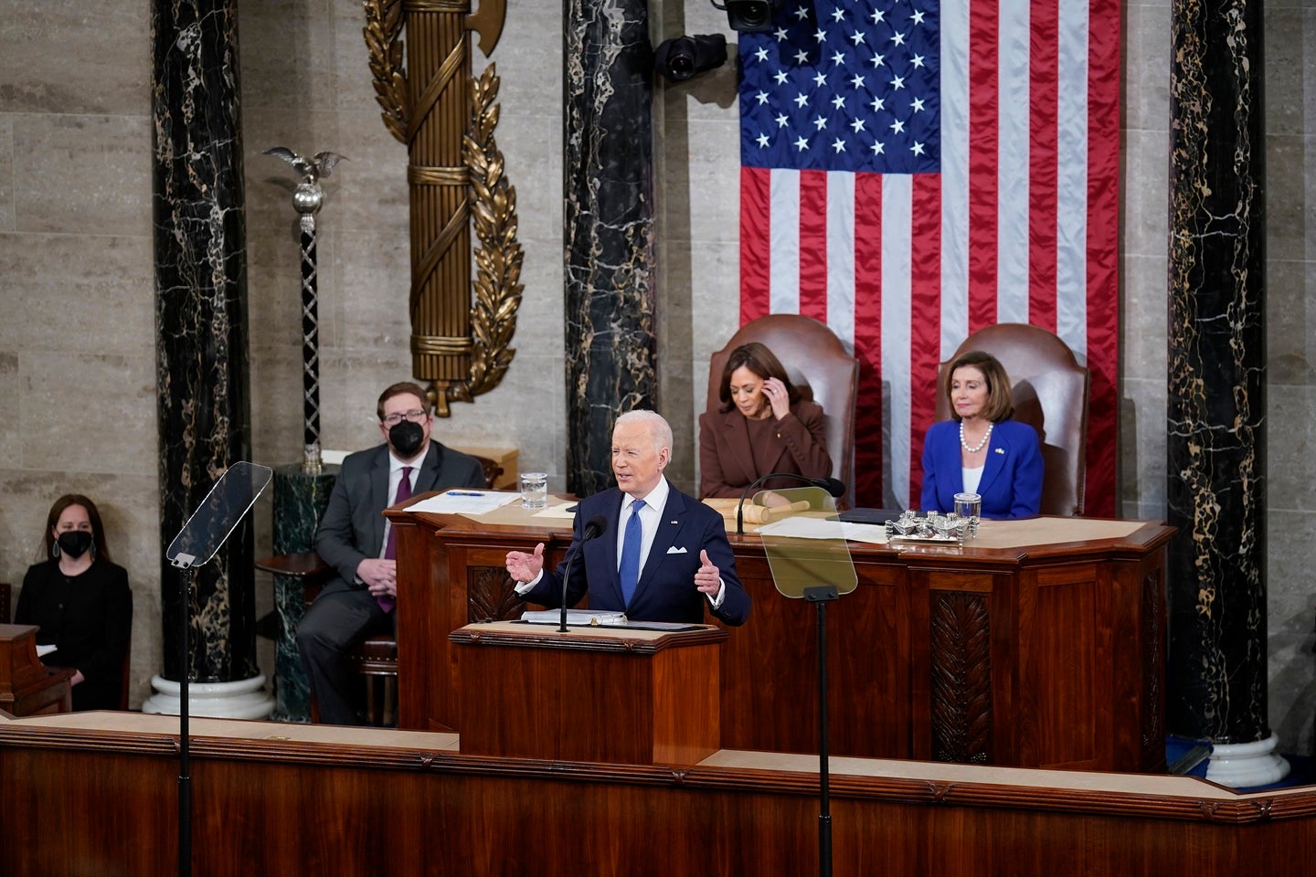 Biden State of the Union 2022 with the US president, vice president, and speaker of the House of Representatives in front of an American flag and two other individuals wearing COVID masks in the Capitol
