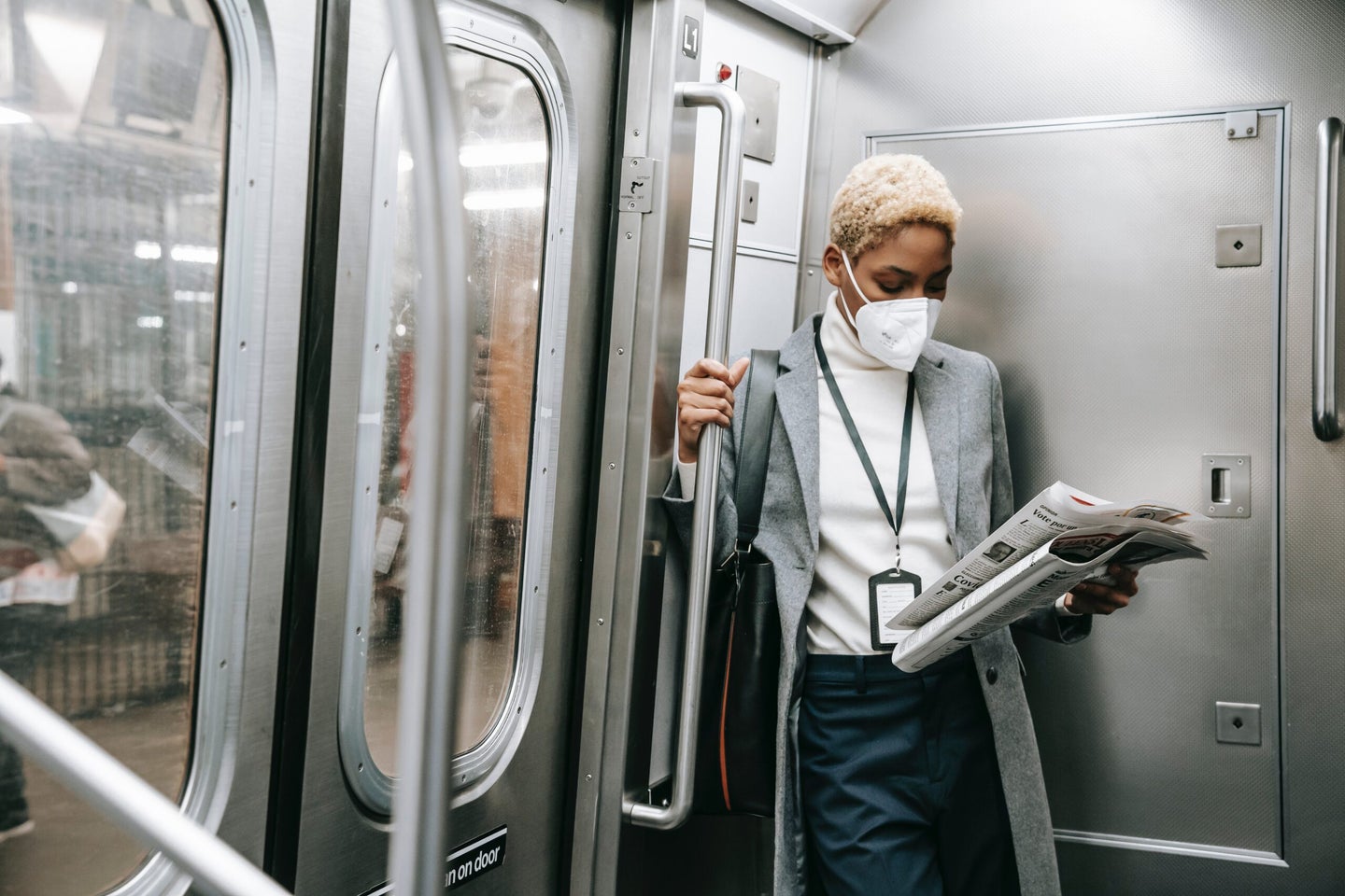 Focused black woman in mask reading newspaper in new york city subway train