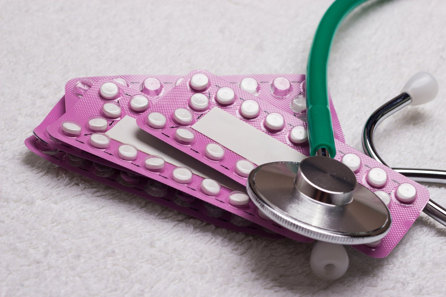 Pink birth controls pills and green stethoscope to symbolize hormone issues