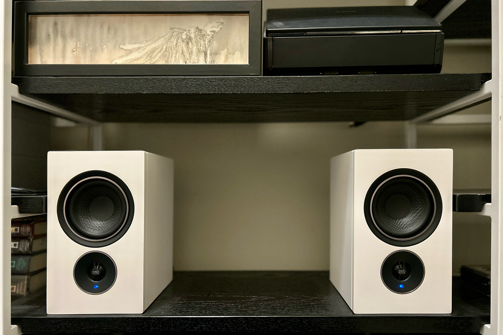 White PSB Alpha iQ speakers on a black shelf