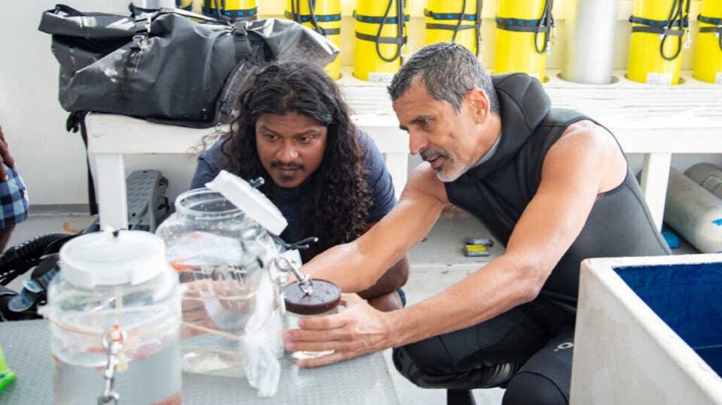 Two researchers in wet suits on a boat looking at a jar of specimens from the twilight zone in the Maldives