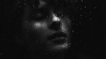 woman in sad mood behind glass with water droplets