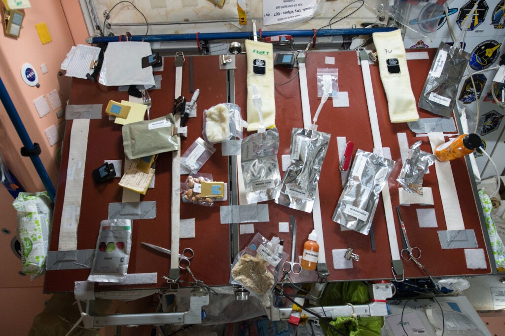 various packets of food, condiments, and drinks are strapped down onto a red table. scissors for cutting packages are also strapped down 