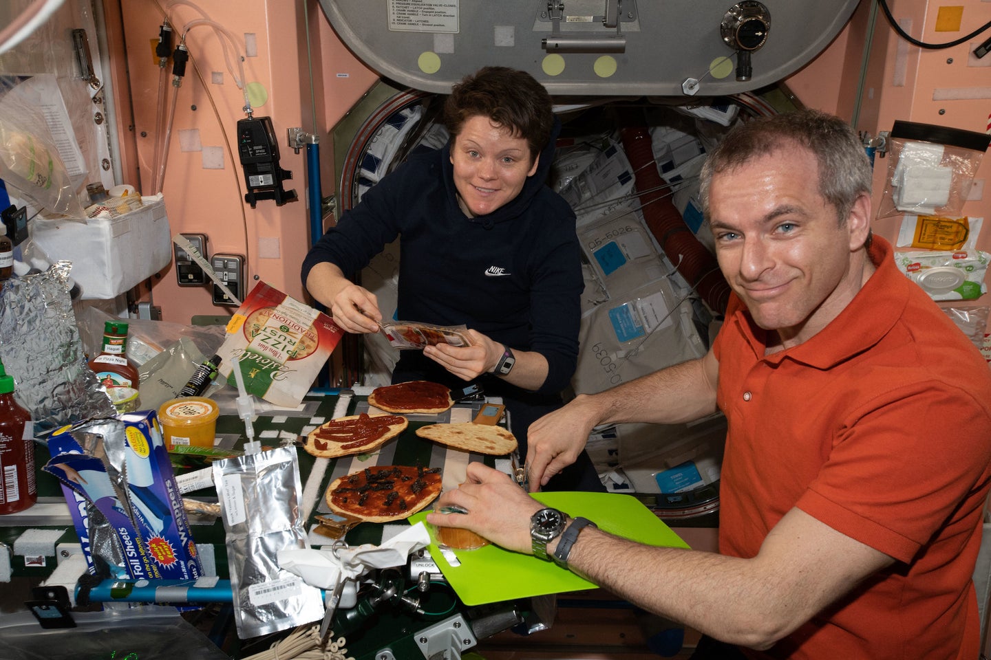 two astronauts in the international space station prepare pizza