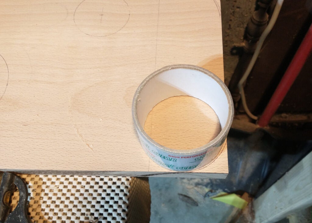 A roll of packing tape lined up against the corner of a piece of wood for tracing a curved corner.