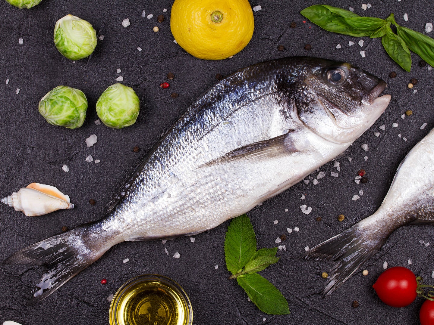 Raw fresh dorado fish with fruits and vegetables to illustrate an article about cleaning fish.