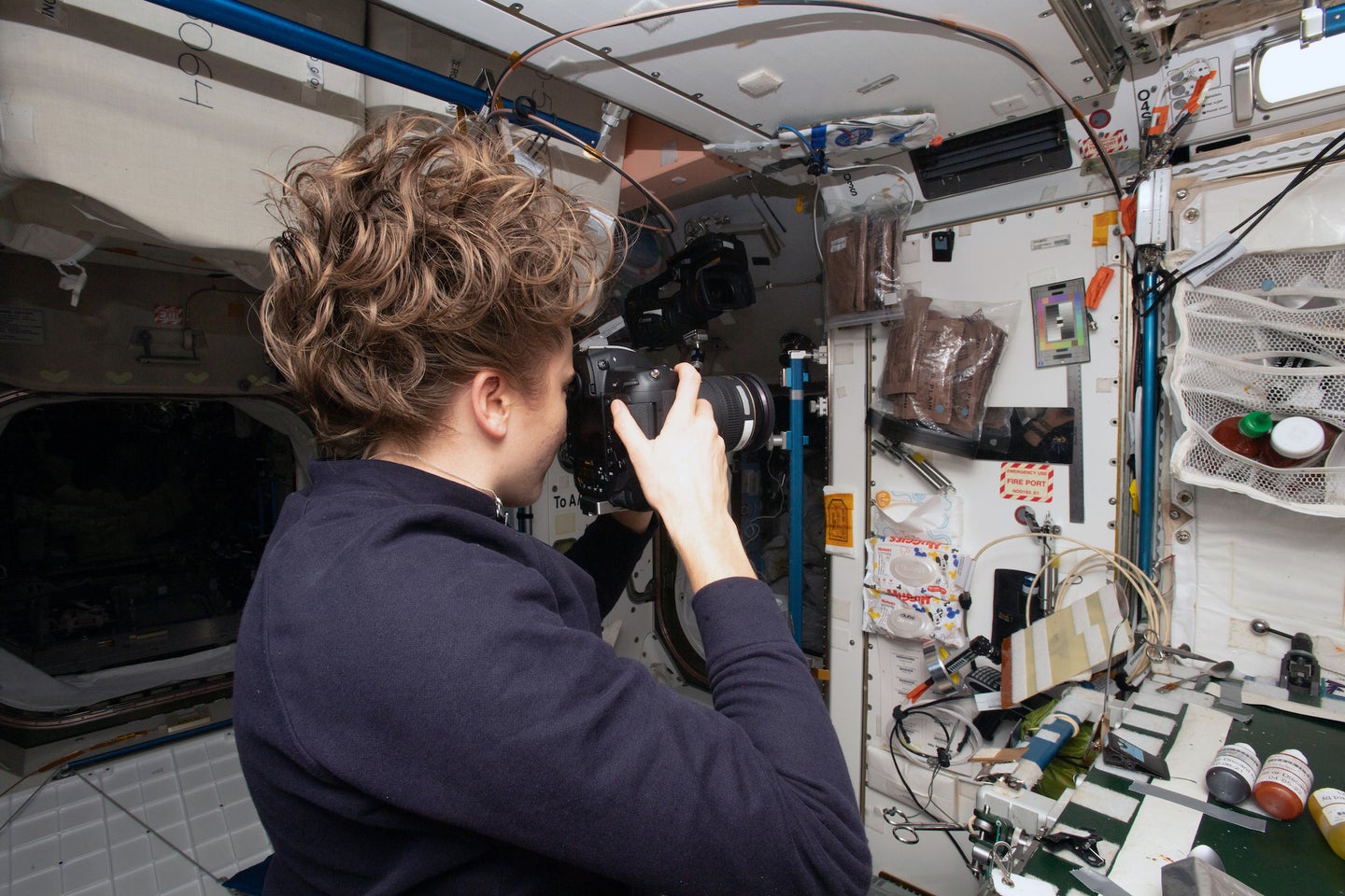 a female astronaut on the international space station takes a picture of section of the station with equipment