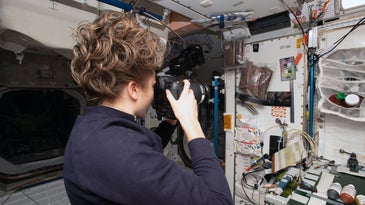a female astronaut on the international space station takes a picture of section of the station with equipment