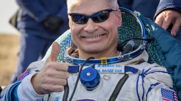 a man wearing sunglasses and a space suit gives a thumbs up after landing back on earth