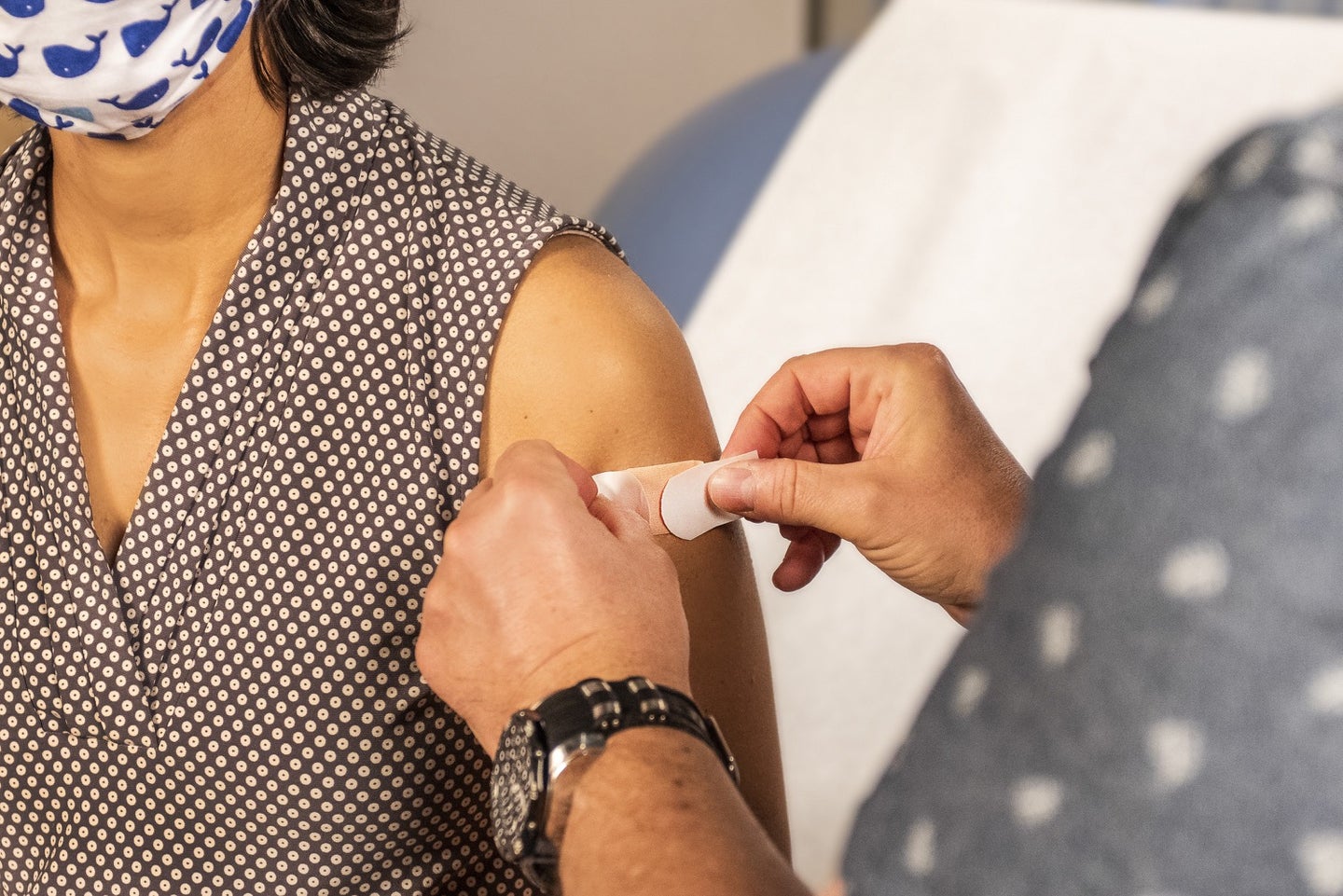 a woman wearing a mask finished receiving a shot and is getting a bandaid on her arm