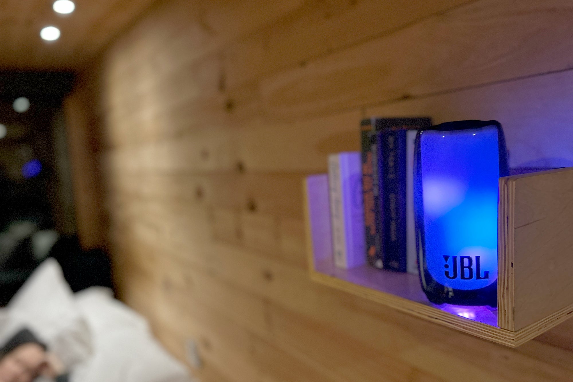JBL Pulse 5 Bluetooth speaker pulsing blue in a getaway cabin