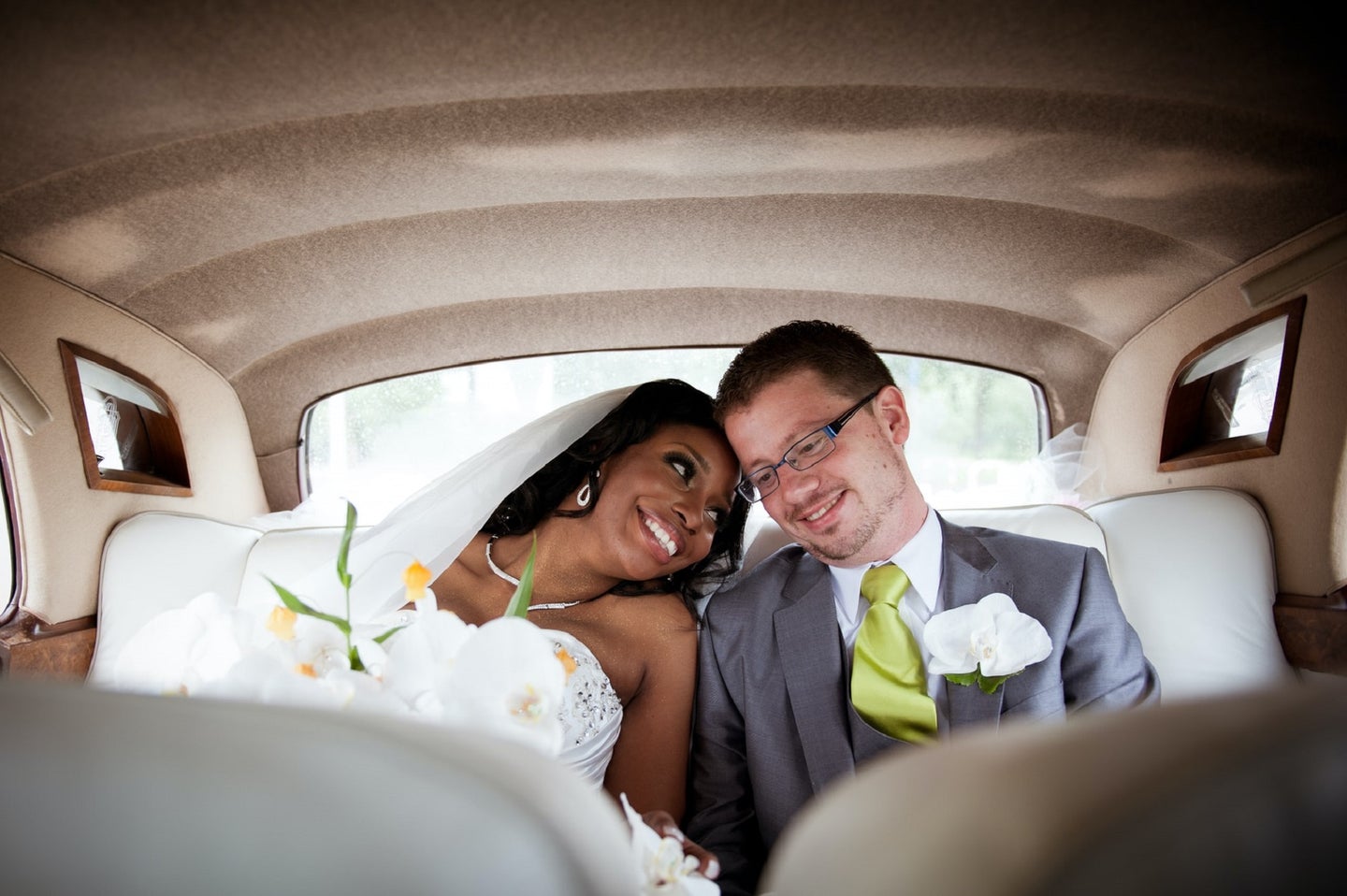 Black bride and white groom in the back seat of a wedding car holding hands and looking in love