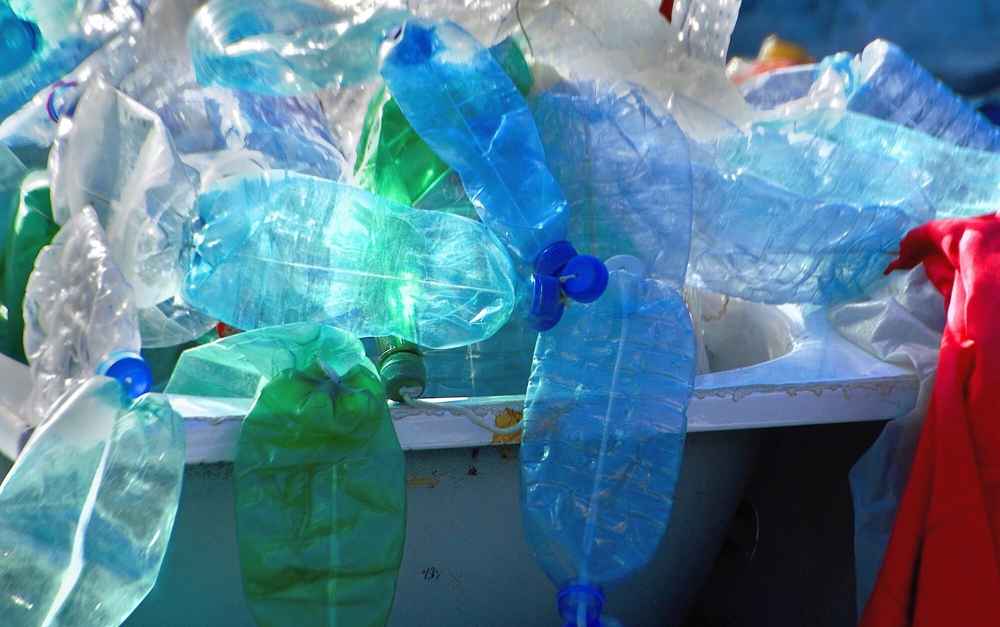 A trash bin is overflowing with blue and green plastic bottles