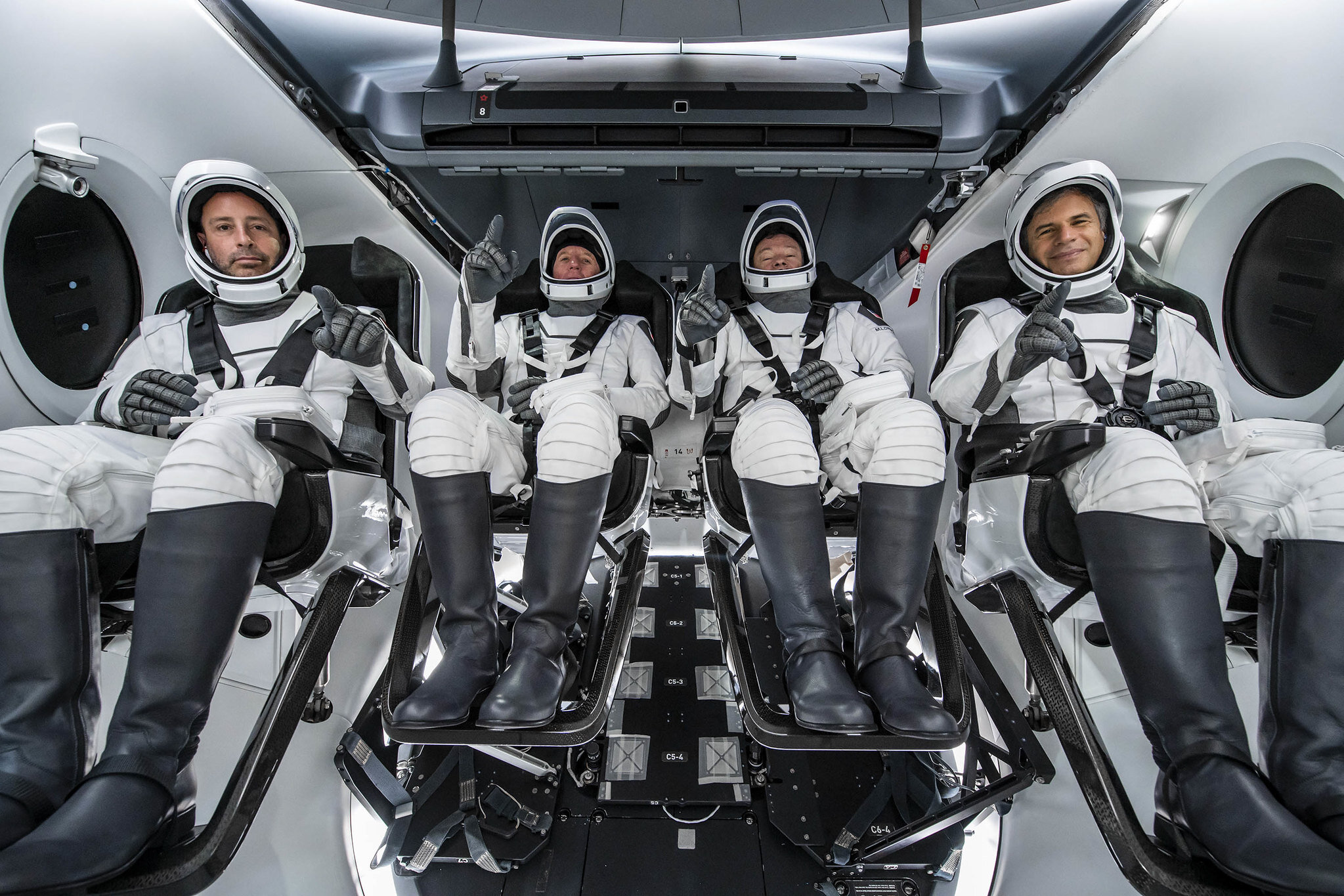 four men sit in spacesuits on a spacecraft