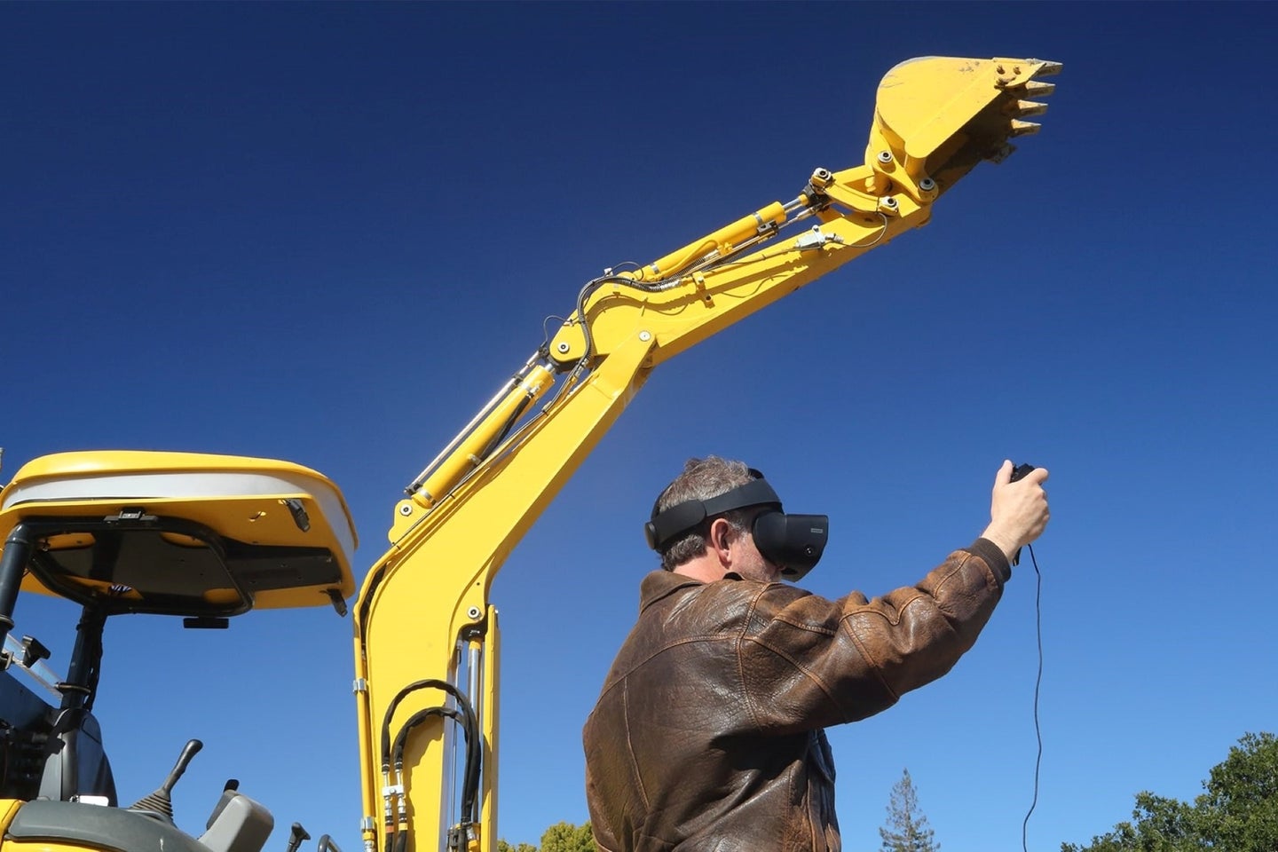 A robotic excavator lifts its scooper as commanded by a user wearing an Oculus headset.