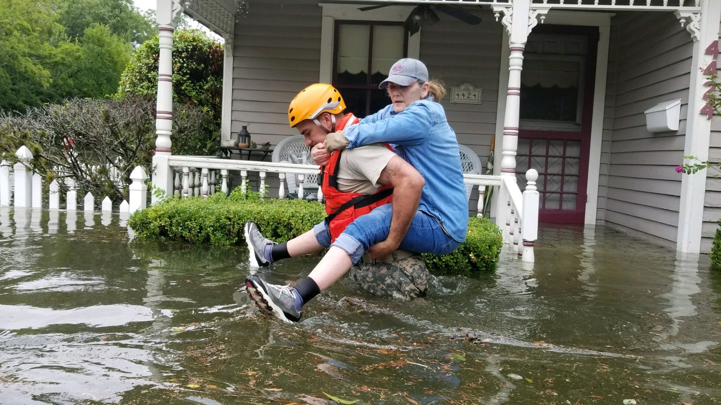 a national guard soldier carries a woman on his back through flooded streets during a hurricane