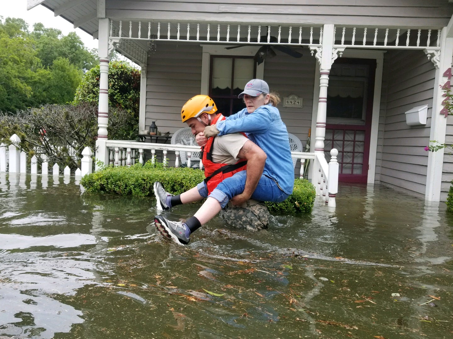a national guard soldier carries a woman on his back through flooded streets during a hurricane