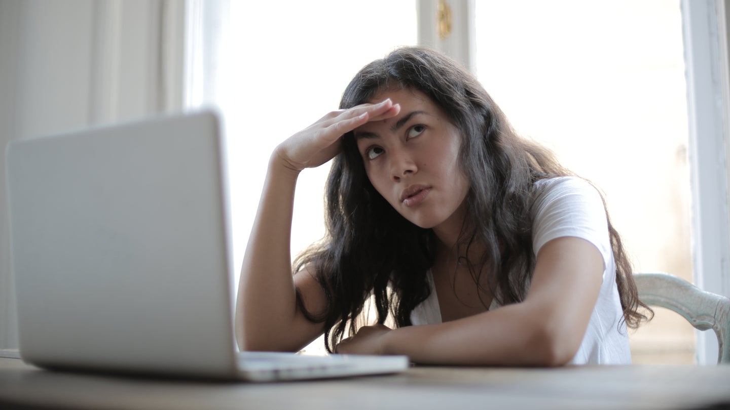 A woman sitting in front of a white laptop looking annoyed.