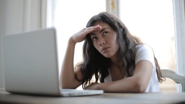 A woman sitting in front of a white laptop looking annoyed.