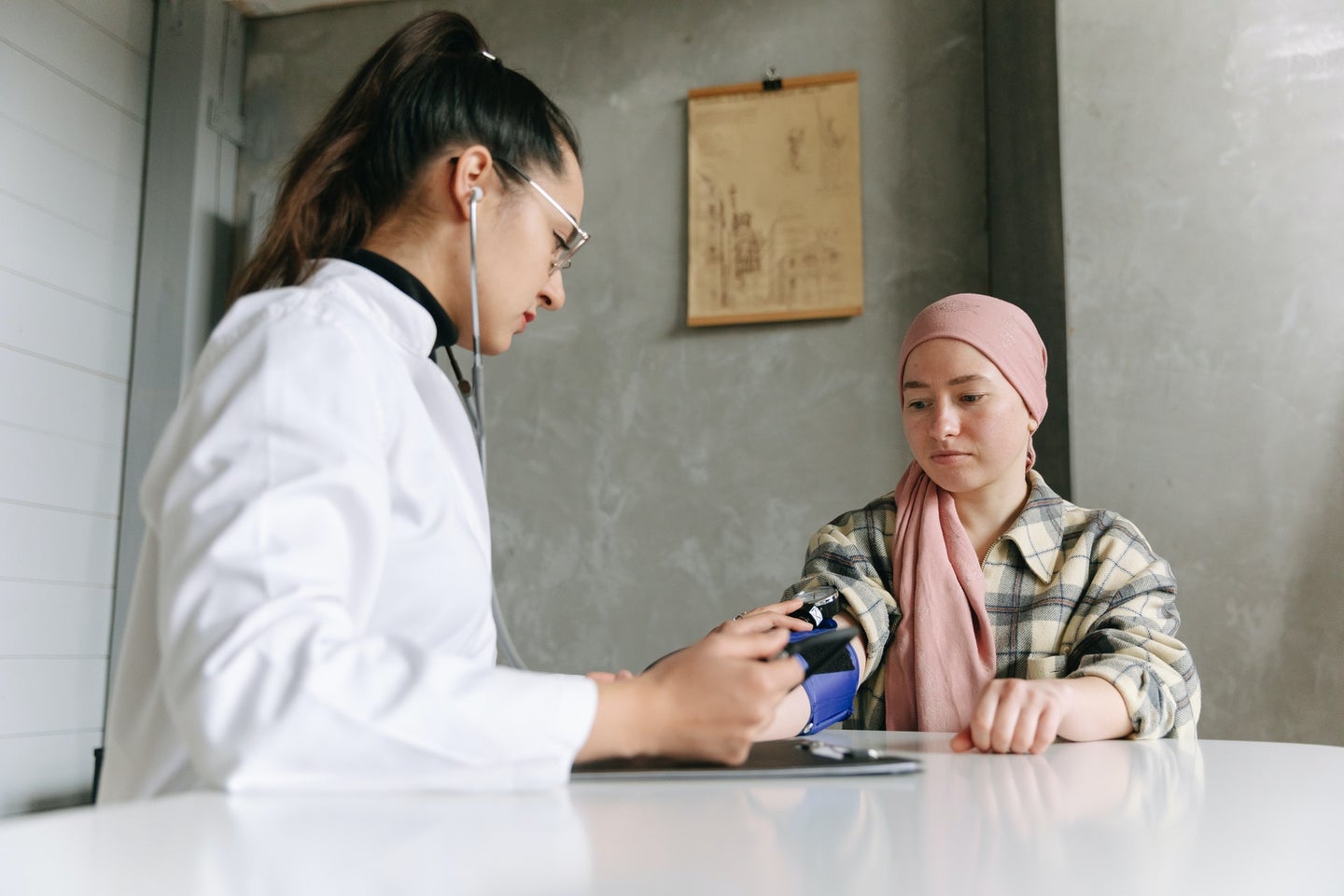 Person in a pink hijab talking to an oncologist in a pony tail and white coat about cancer treatments