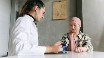 Person in a pink hijab talking to an oncologist in a pony tail and white coat about cancer treatments