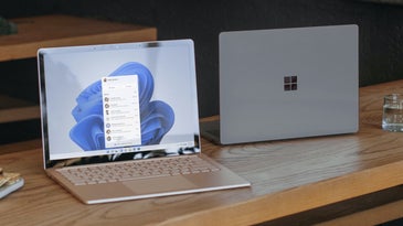 Two Windows laptops on a long wooden table, facing opposite directions. You can see the screen of one, but not the other.