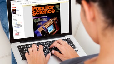 A woman wearing a gray shirt and blue jeans using a laptop on her lap with the Popular Science archive on the screen.