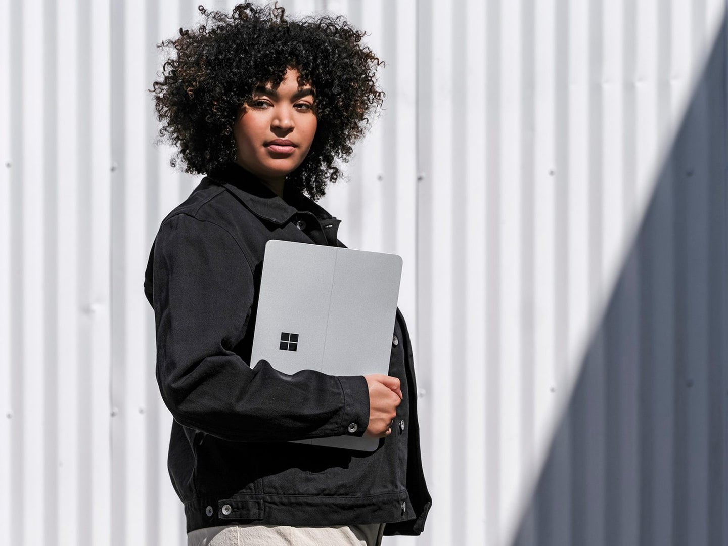 A person holding a Windows 11 tablet while standing outside near a gray background on a sunny day.