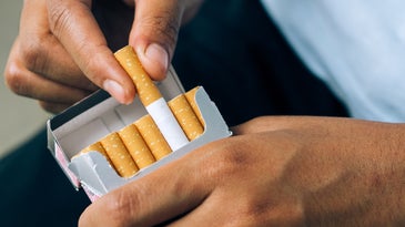 a close up of a person pulling a cigarette out of a pack