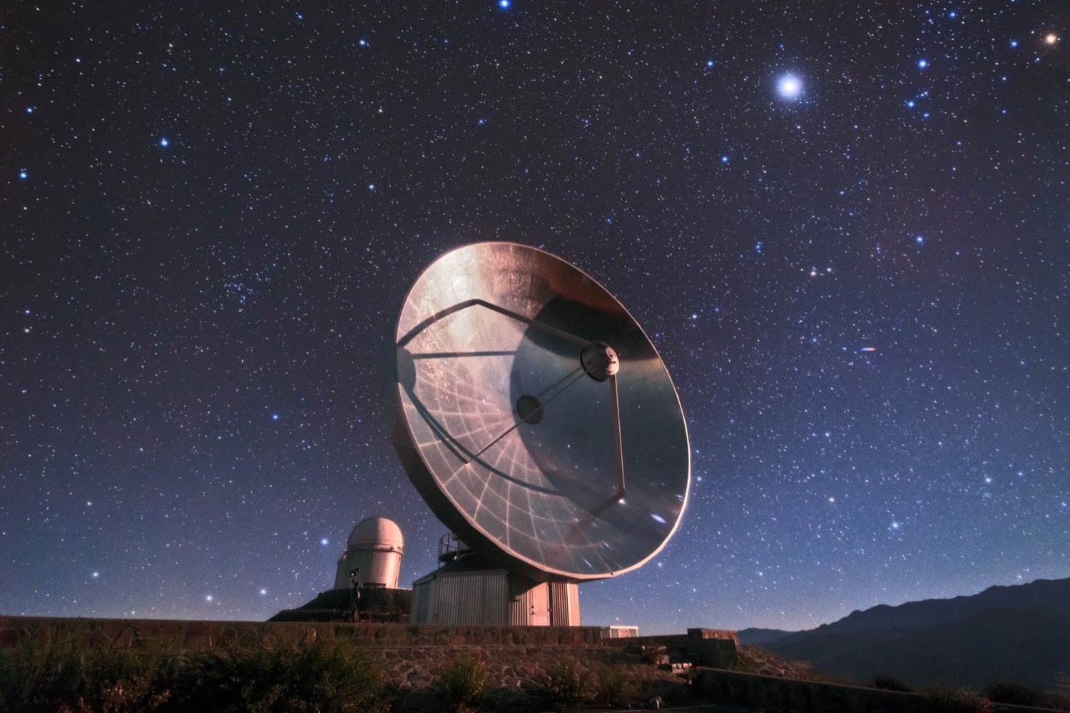 a large silver dished radio telescope that gleams under a star-studded night sky