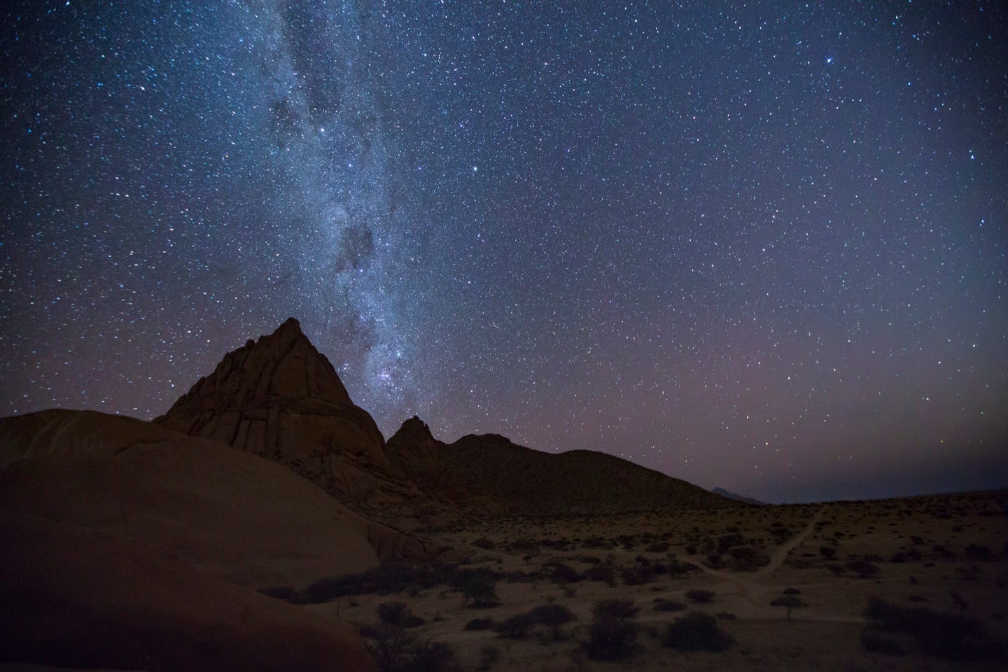 a beautiful night sky over a desert is glistening with stars, and the streak of the milky way galaxy stretches across