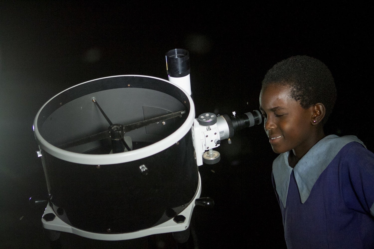 a young kenyan girl looks through a telescope at night
