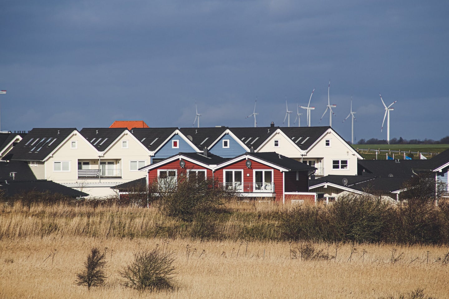 Grass field with homes and wind turbines in the background.